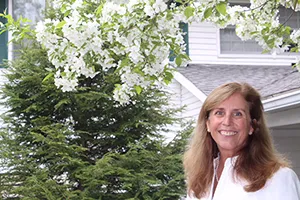 A woman standing in front of a tree with white flowers.