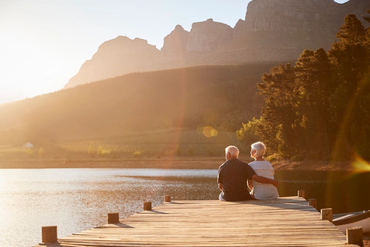 A man and woman sitting on the dock of a lake.